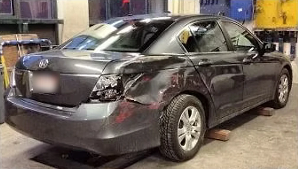 Grey sedan with a crushed rear quarter panel and bumper before repair