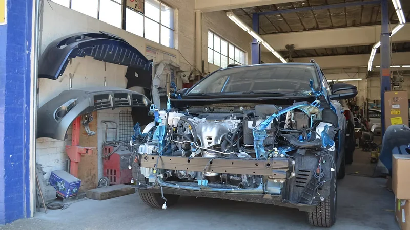 A vehicle with its front bumper removed in the Quincy Auto Body shop bay, with replacement bumper covers waiting alongside